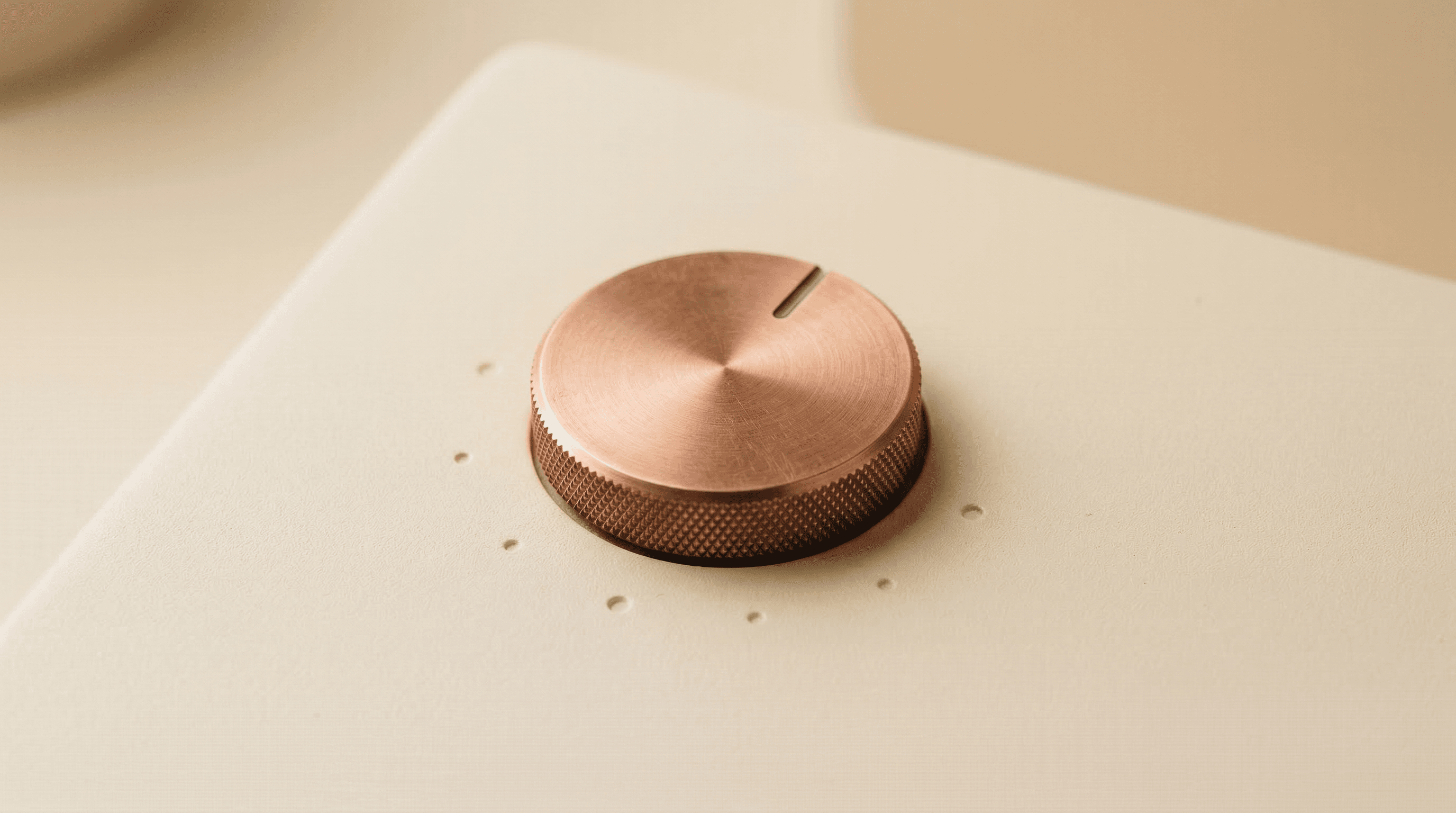 A minimalist control dial with copper finish on cream surface, suggesting levels of precision and control